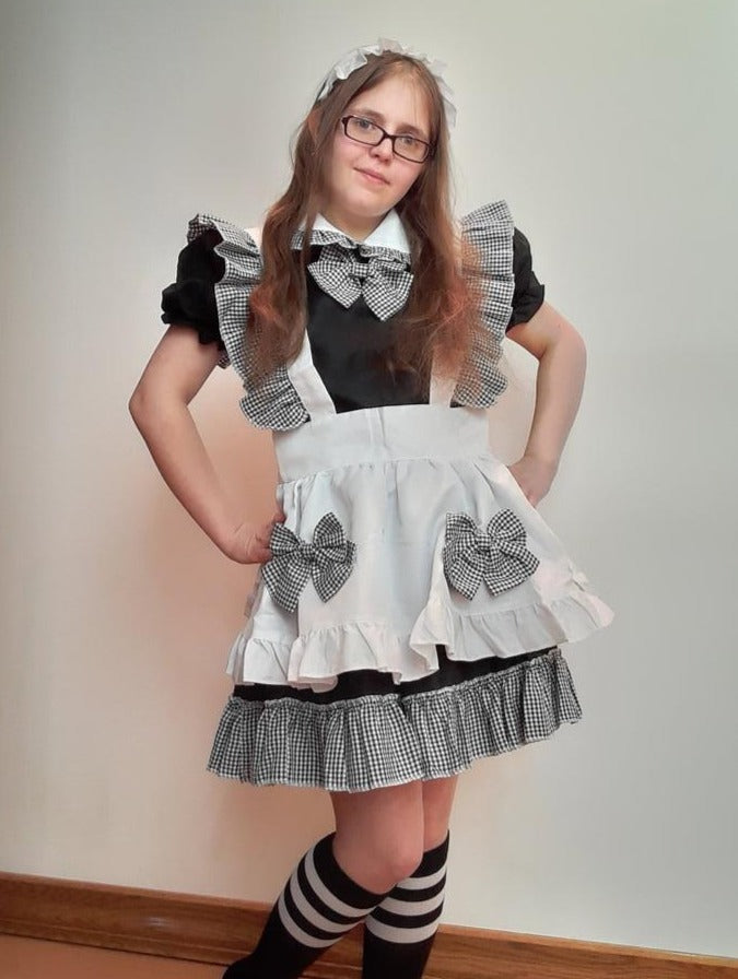 Woman in a black and white maid cosplay outfit with bows, ruffles, and striped knee-high socks