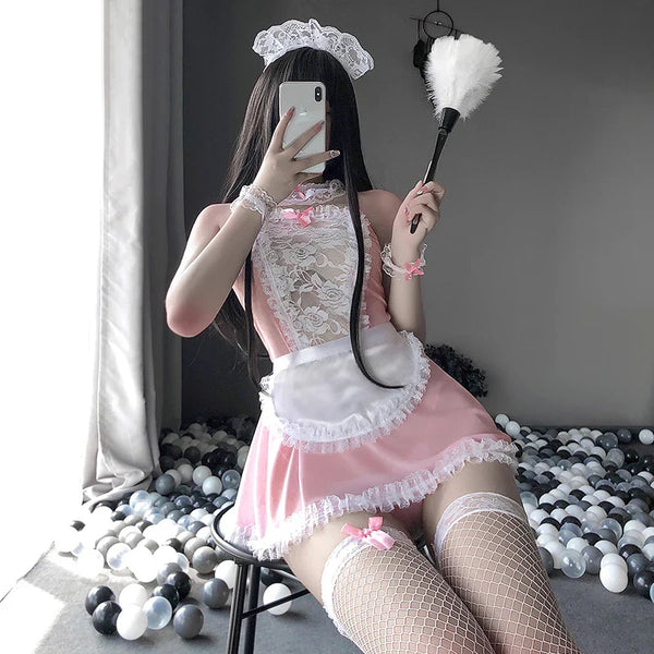 Woman in a pink and white maid costume taking a selfie while holding a feather duster.