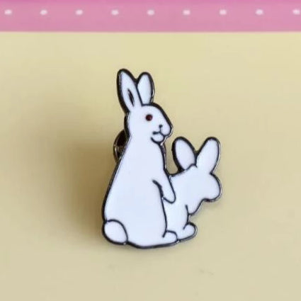 Enamel pin depicting two white rabbits in a playful pose.