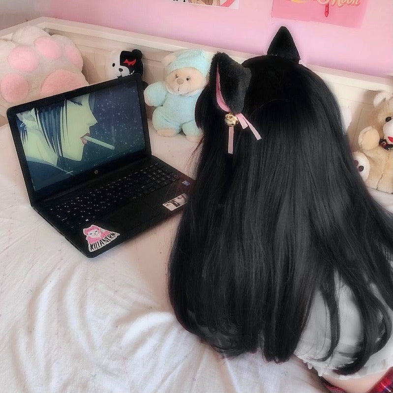 Person with long black hair wearing cat ears, sitting on a bed and watching a laptop.