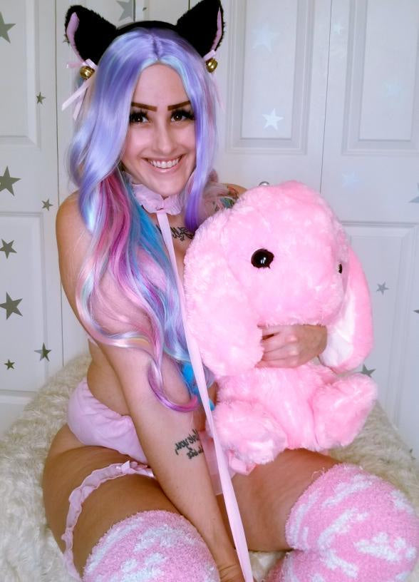 Woman with colorful hair wearing cat ears and holding a pink plush toy.